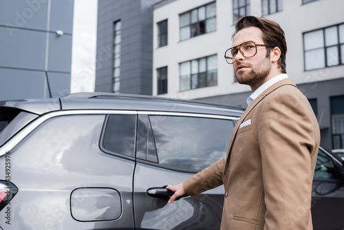 young businessman in beige suit reaching car door