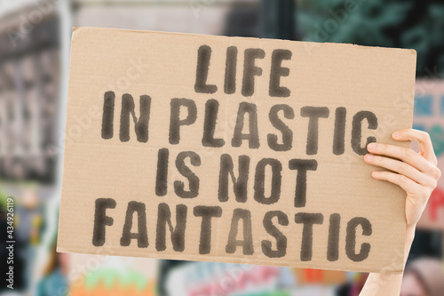 The phrase " Life in plastic is not fantastic " on a banner in men's hand. Human holds a cardboard with an inscription. Sustainable. Recyclable. Unhygienic. Reuse. Container. Consumerism © AndriiKoval