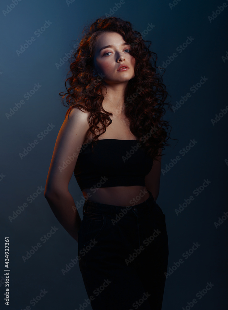 Beauty young woman with curly big and long hair. Glamour lady on dark blue background. Cute woman face wavy hair, perfect make up, red lips Beauty young woman with curly big and long hair. Glamour lady on dark blue background. Cute woman face wavy hair, perfect make up, red lips