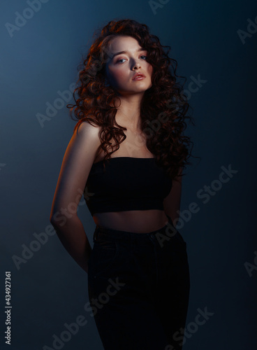 Beauty young woman with curly big and long hair. Glamour lady on dark blue background. Cute woman face wavy hair, perfect make up, red lips