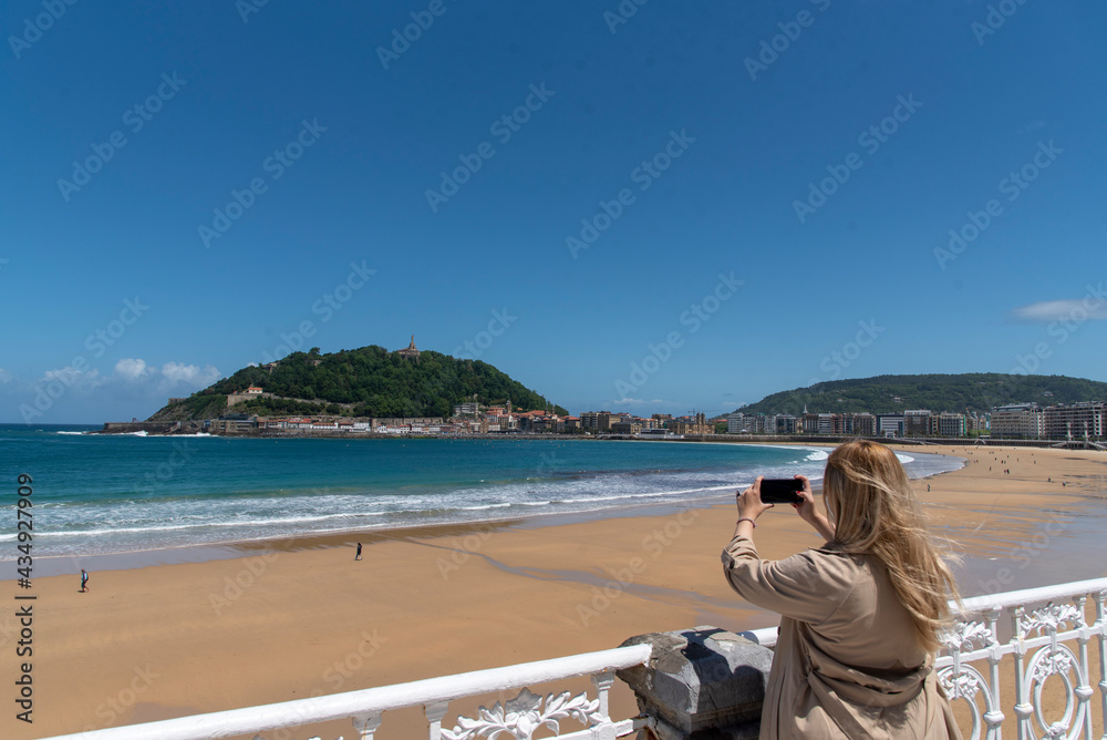 mujer rubia sacando una foto con el móvil en la playa de la concha en San Sebastian, Guipuzcoa. 