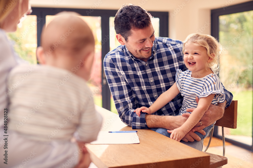 Smiling Family Sitting Around Kitchen Counter At Home Together Smiling Family Sitting Around Kitchen Counter At Home Together