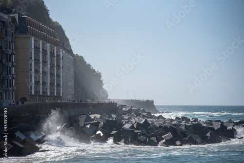 Edificios de la costa de San Sebastián en un día despejado y con la bruma del mar y olas ola chocando en el rompeolas photo