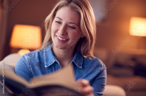 Woman At Home Relaxing And Reading Book Sitting On Sofa In Evening