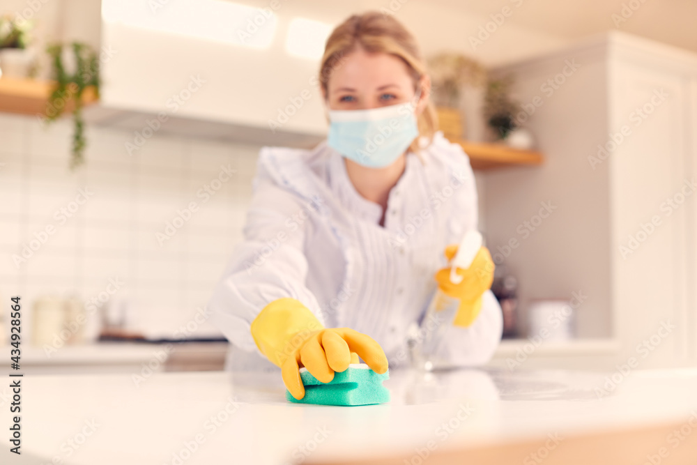 Woman At Home Wearing Mask In Kitchen Doing Housework And Cleaning Counter Surface With Spray