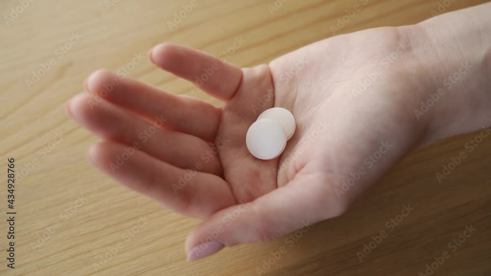 Two white pills fall on a woman palm from bottle of pills. Close-up. Two white pills fall on a woman palm from bottle of pills. Close-up.