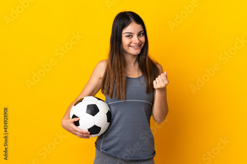 Young football player woman isolated on yellow background making money gesture © luismolinero