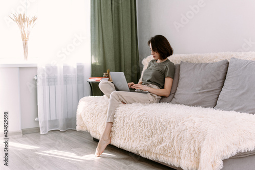 Enjoying time at home. Beautiful young smiling woman working on laptop sitting in a comfortable sofa at home