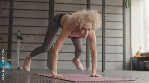 Locked-down of young strong Caucasian woman wearing sports clothing, doing burpee exercise in gym at daytime photo