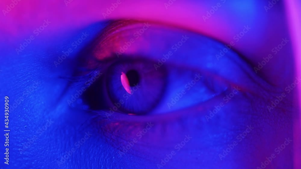 Extreme close up of human eye iris under neon light 4K. Female with beautiful makeup, glitter shadows and false lashes. Womens green eye contracting. Nightlife, night club concept. Extreme close up of human eye iris under neon light 4K. Female with beautiful makeup, glitter shadows and false lashes. Womens green eye contracting. Nightlife, night club concept.