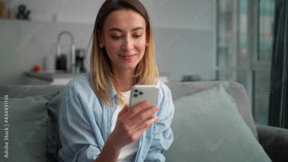 The positive woman typing something on the phone while sitting on the couch in the room The positive woman typing something on the phone while sitting on the couch in the room