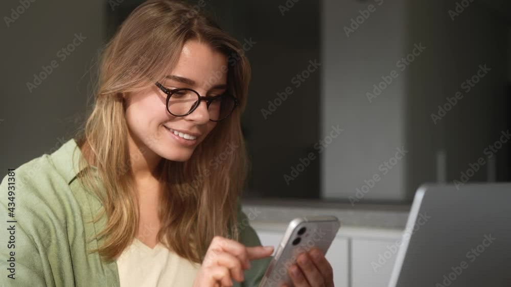 The smiling woman typing on the phone while sitting at the home The smiling woman typing on the phone while sitting at the home