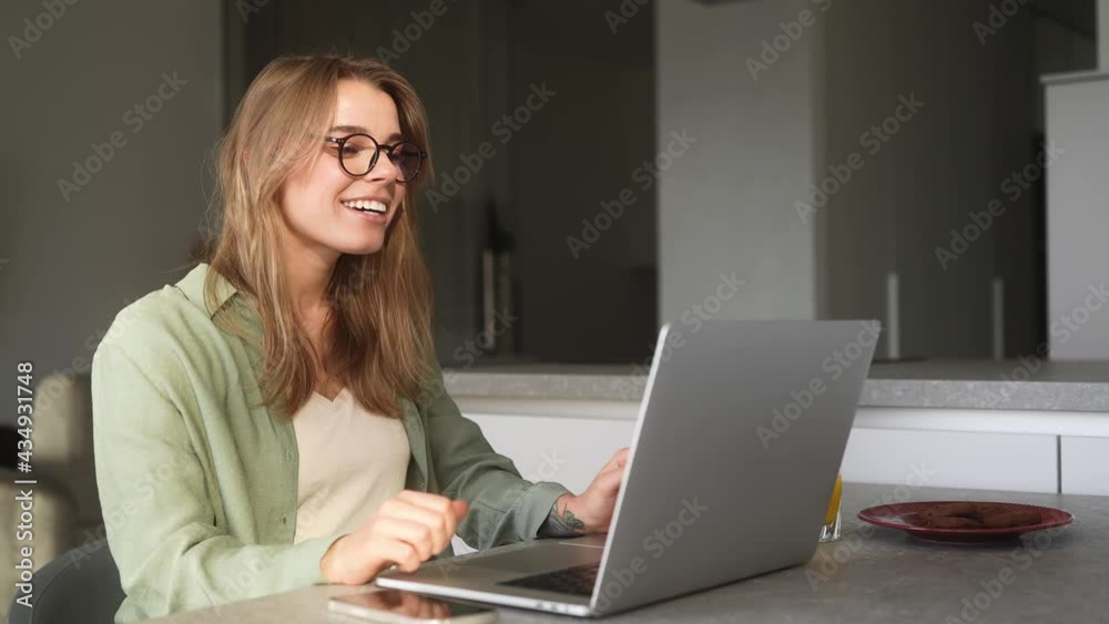 The happy woman talking by video call on laptop and waving to his camera while sitting in the room The happy woman talking by video call on laptop and waving to his camera while sitting in the room