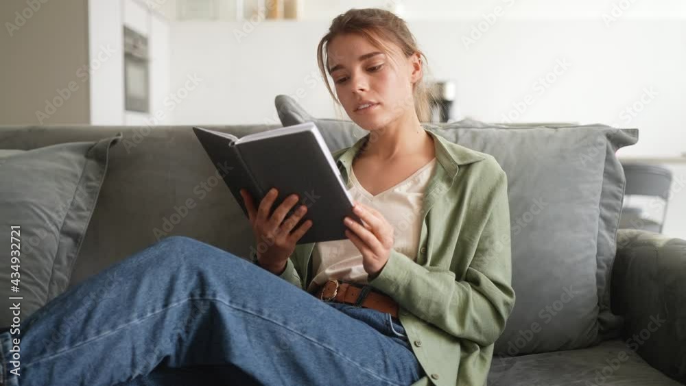 A side-view of a laughing woman reading book while sitting on the sofa in the room A side-view of a laughing woman reading book while sitting on the sofa in the room