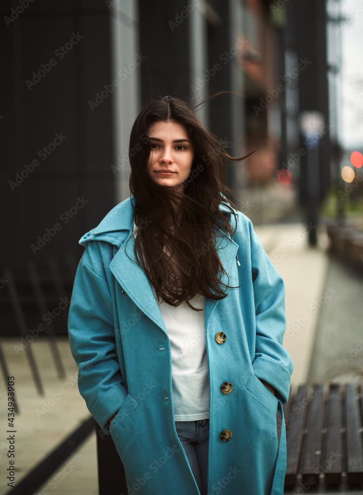 A gorgeous woman with long dark hair looking into the camera. Brunette and windy weather. Alone stunning girl in the downtown with bokeh city lights in the background.