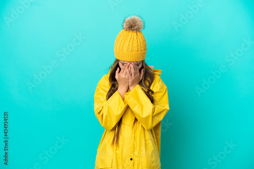 Little girl wearing a rainproof coat over isolated blue background with tired and sick expression