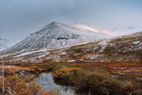 Autumn tundra and cold river on the background of misty snow-capped mountains, Arctic, Kola Peninsula