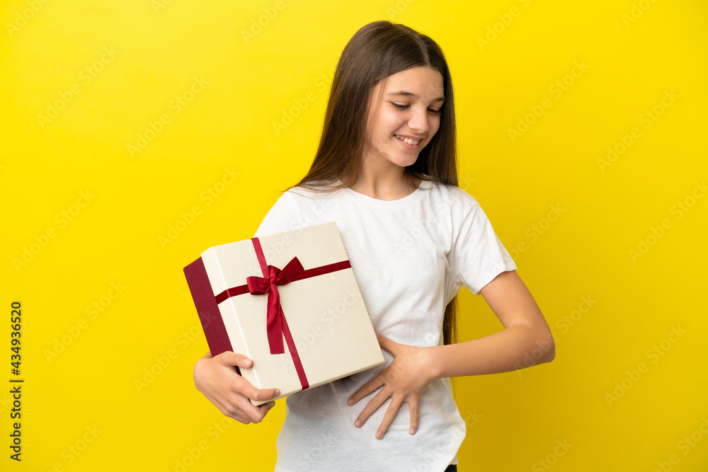 Little girl holding a gift over isolated yellow background smiling a lot Little girl holding a gift over isolated yellow background smiling a lot