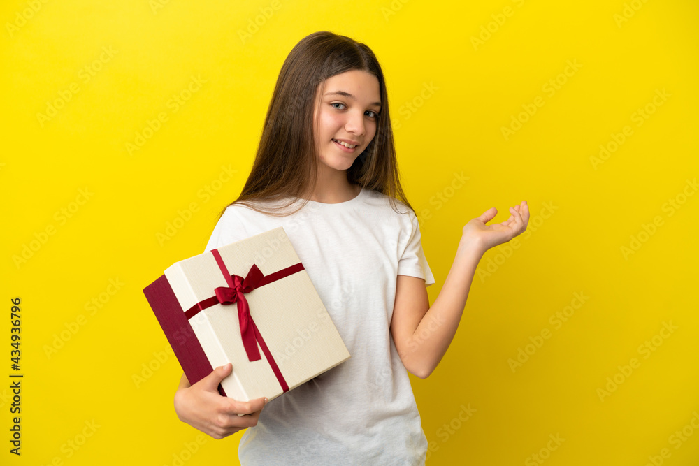 Little girl holding a gift over isolated yellow background extending hands to the side for inviting to come Little girl holding a gift over isolated yellow background extending hands to the side for inviting to come