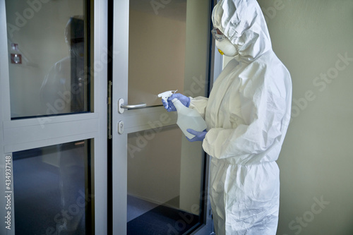 Person in protective suit disinfecting door in the public building © gpointstudio