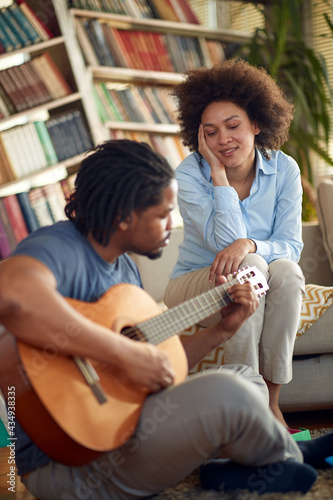 A young man plays the guitar for his wife at home. Family, together, love, music