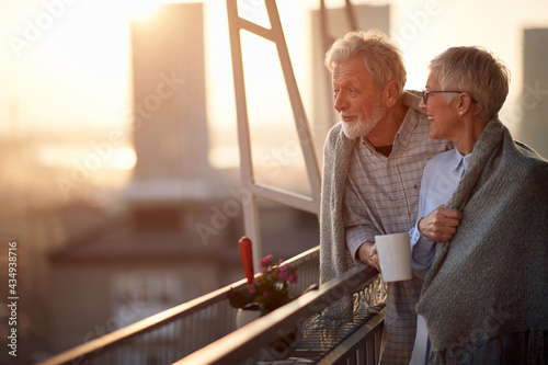 An elderly couple enjoying a view on the city from the terrace of their appartment. Spouses, pensioners, together, home