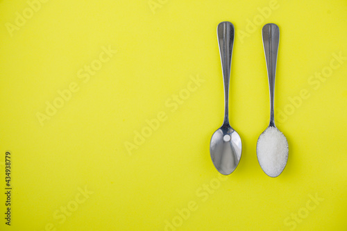 Sugar-replacement tablet of stevia and sugar in tea spoons lying in same directions on bright yellow paper background. Horizontal, copy space, flat lay top view