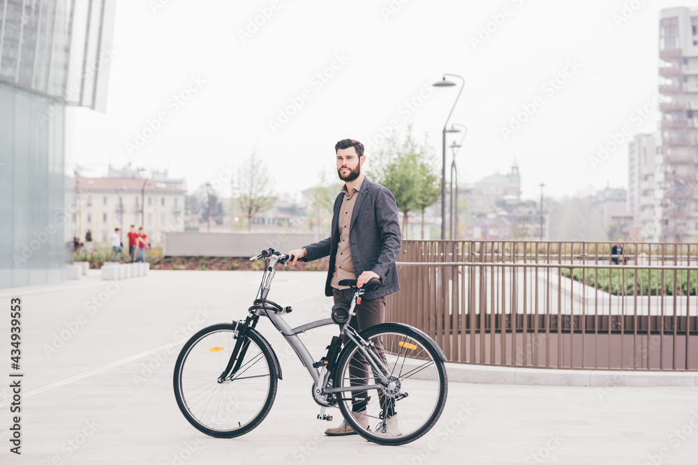Young contemporary bearded businessman posing outdoor holding bike smiling Young contemporary bearded businessman posing outdoor holding bike smiling