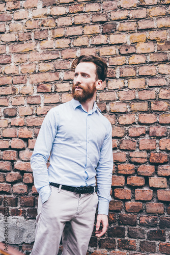 Young bearded business man outdoor leaning brick wall looking away pensive