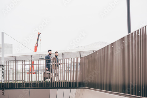 Two young casual businessmen walking outdoor chatting going to work
