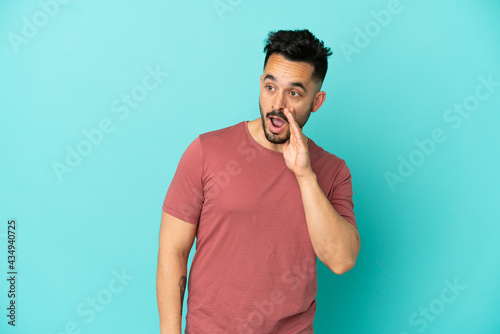 Young caucasian man isolated on blue background whispering something with surprise gesture while looking to the side