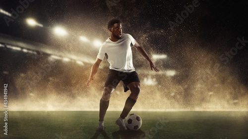 Professional male football, soccer player on stadium background. African fit athlete practicing, playing excited