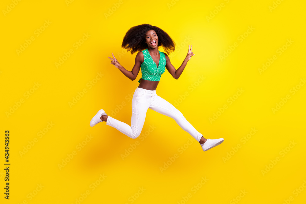 Full length body size photo young girl jumping showing v-sign gesture isolated vivid yellow color background