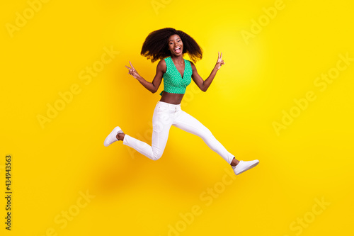 Fototapeta Naklejka Na Ścianę i Meble -  Full length body size photo young girl jumping showing v-sign gesture isolated vivid yellow color background