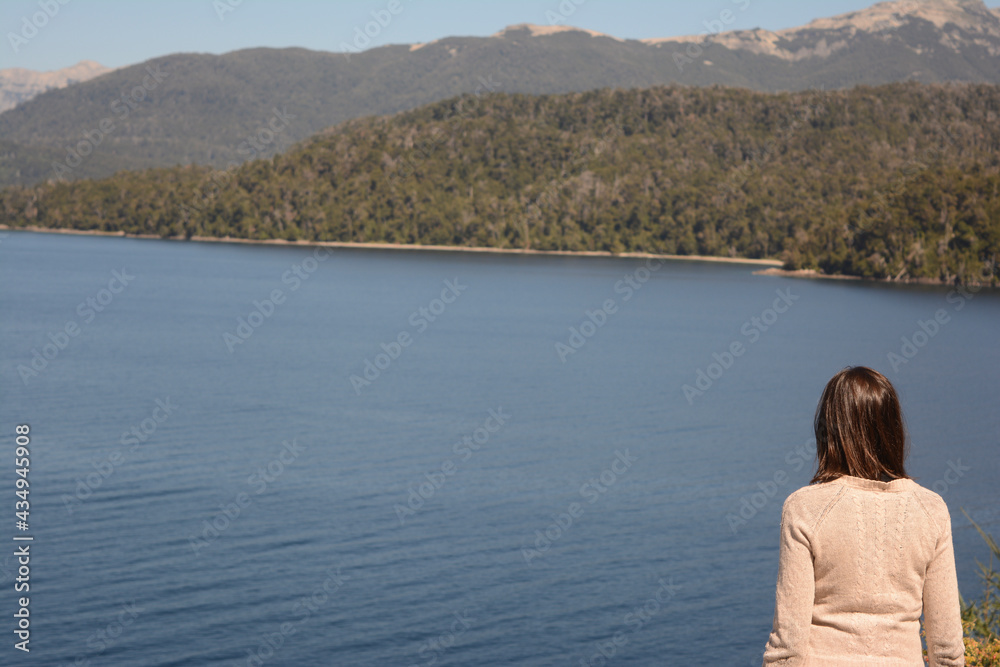 woman with her back turned on the shores of a pensive lake with mountains