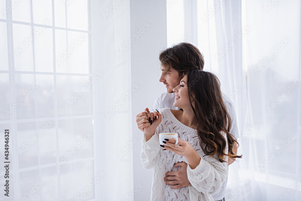 Side view of man holding hand of smiling girlfriend with coffee at home Side view of man holding hand of smiling girlfriend with coffee at home
