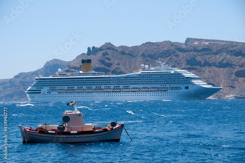 A cruise ship and a fishing boat sailing in the caldera of the island of Santorini in Greece. In the background the coast of Thirasia