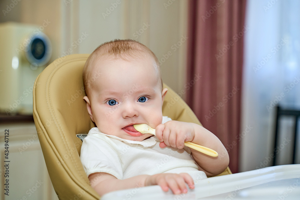 a small child with blue eyes is holding a spoon sitting in a high chair. a small child with blue eyes is holding a spoon sitting in a high chair.