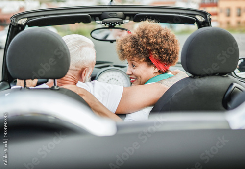 Trendy mulitracial senior couple having fun inside convertible car - Mature people on a road trip in summer vacation with cabriolet car photo