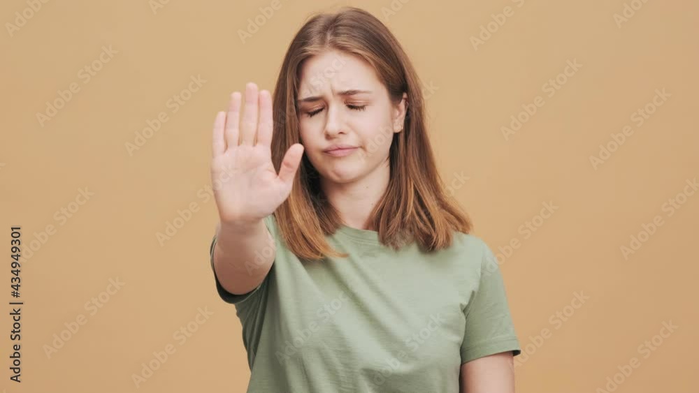 A confident young woman is doing stop gesture standing isolated over a beige wall in the studio A confident young woman is doing stop gesture standing isolated over a beige wall in the studio
