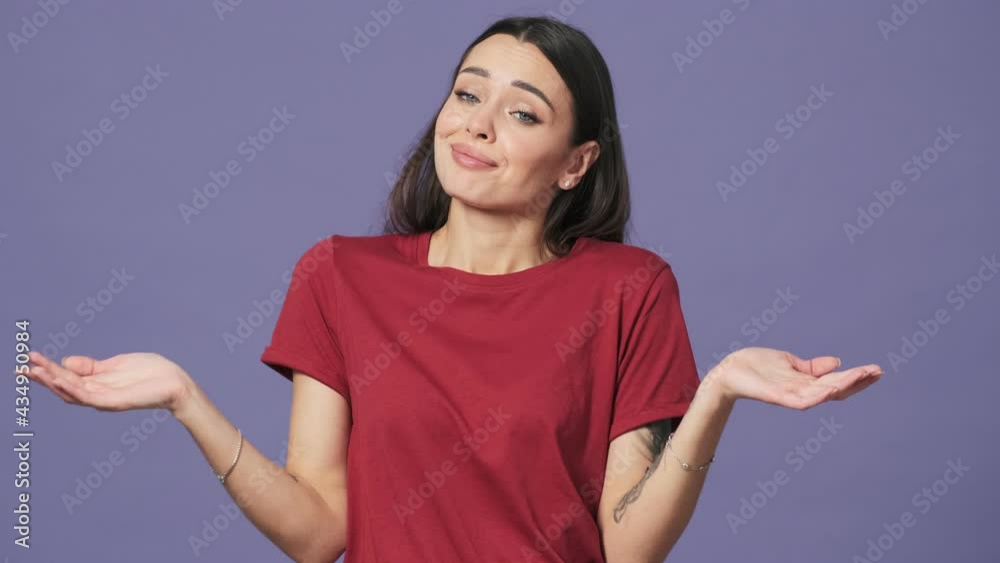 A confused young woman is shrugging her shoulders standing isolated over a purple background in the studio A confused young woman is shrugging her shoulders standing isolated over a purple background in the studio