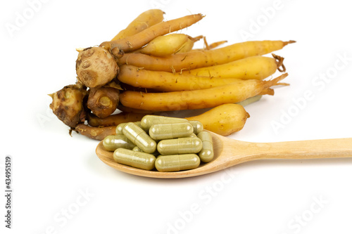 Finger root (Krachai) capsule on wooden spoon isolated on white background. The scientific name is Boesenbergia rotunda. Finger root is herb and Thai food ingredient.