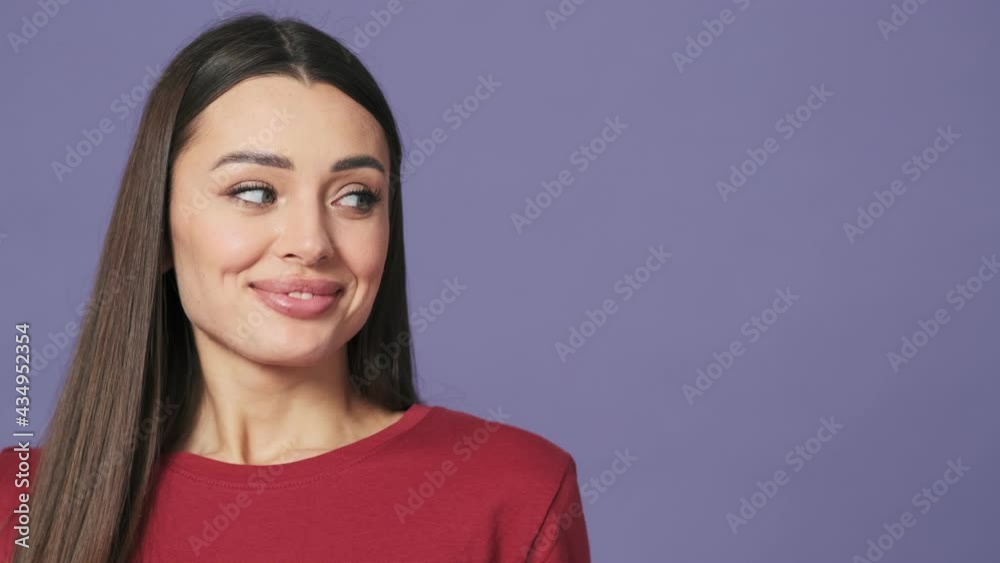 A surprised young woman is looking to the free-space standing isolated over a purple background in the studio A surprised young woman is looking to the free-space standing isolated over a purple background in the studio