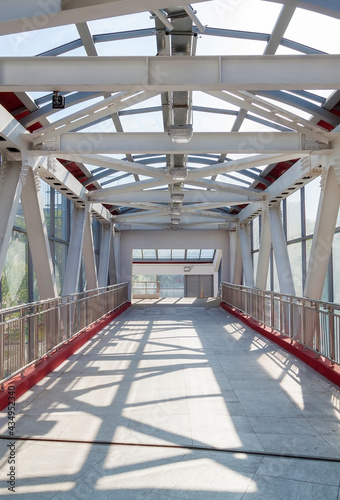 Pedestrian crosswalk under glass roof passage in urban environment. Overhead pedestrian bridge overpass in urban area. Footbridge tunnel made from piles and glass with abstract design