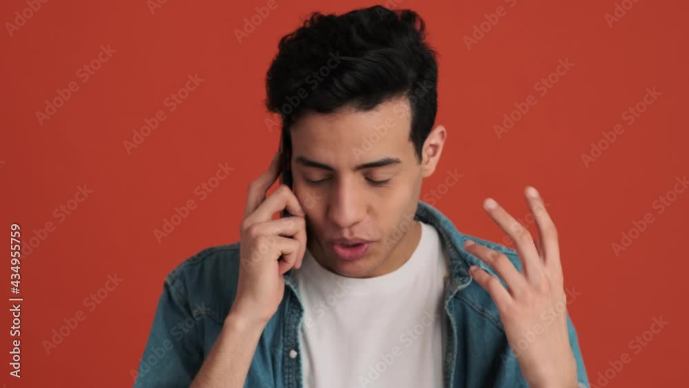The Arab man speaking angrily on the phone and actively gesturing with his hands in an orange studio The Arab man speaking angrily on the phone and actively gesturing with his hands in an orange studio
