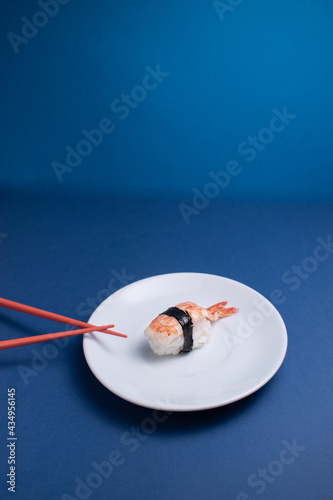 Vertical photograph of a shrimp sushi on a white plate and blue background.
