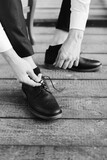 
Black and white photography. A young man puts on black shoes and ties the laces, close-up of male hands. Selective focus.