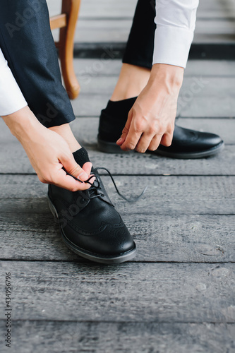 Young man puts on black shoes and ties laces, close-up of male hands. Selective focus.