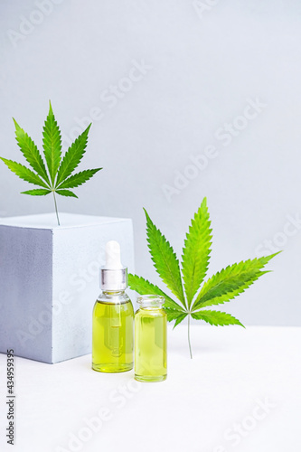 Cosmetics CBD oil and leaves of cannabis. Modern still life of glass bottles with Hemp oil, THC tincture, hemp leaves and cube geometric shape 