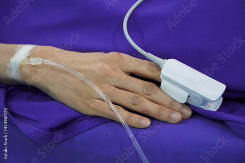 a pulse oximeter for measuring the oxygen content of the blood is attached to a patient's finger. Patient is on a drip receiving a saline solution. 